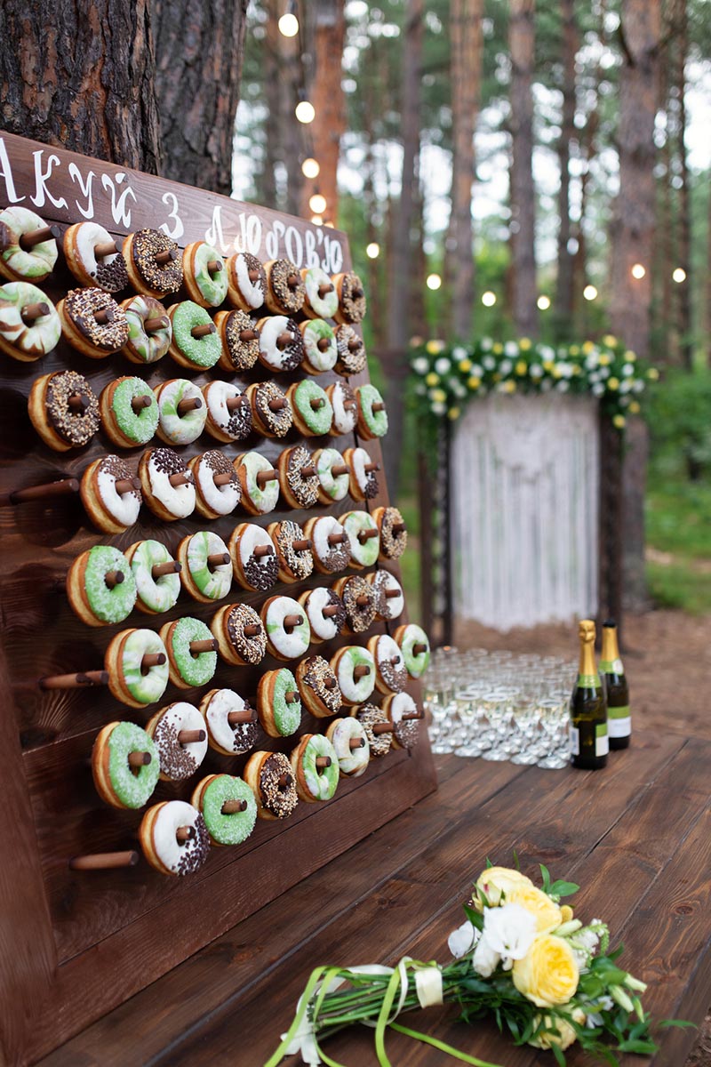 Delicious donuts on wooden stander. Wedding in the forest. Wedding decor. Donuts for guests